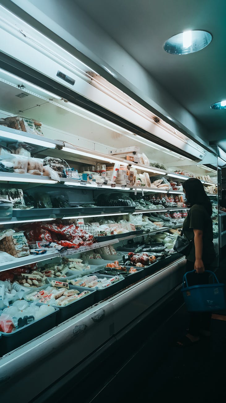 anonymous woman choosing food near fridge in supermarket