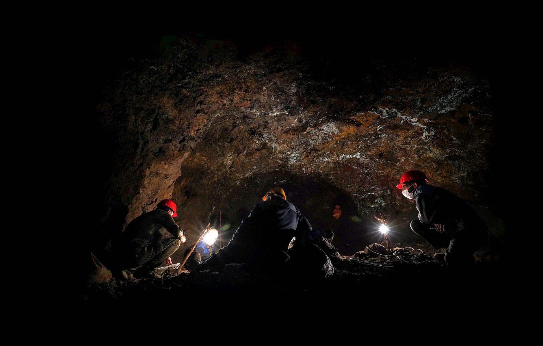 men in helmets by cave at night