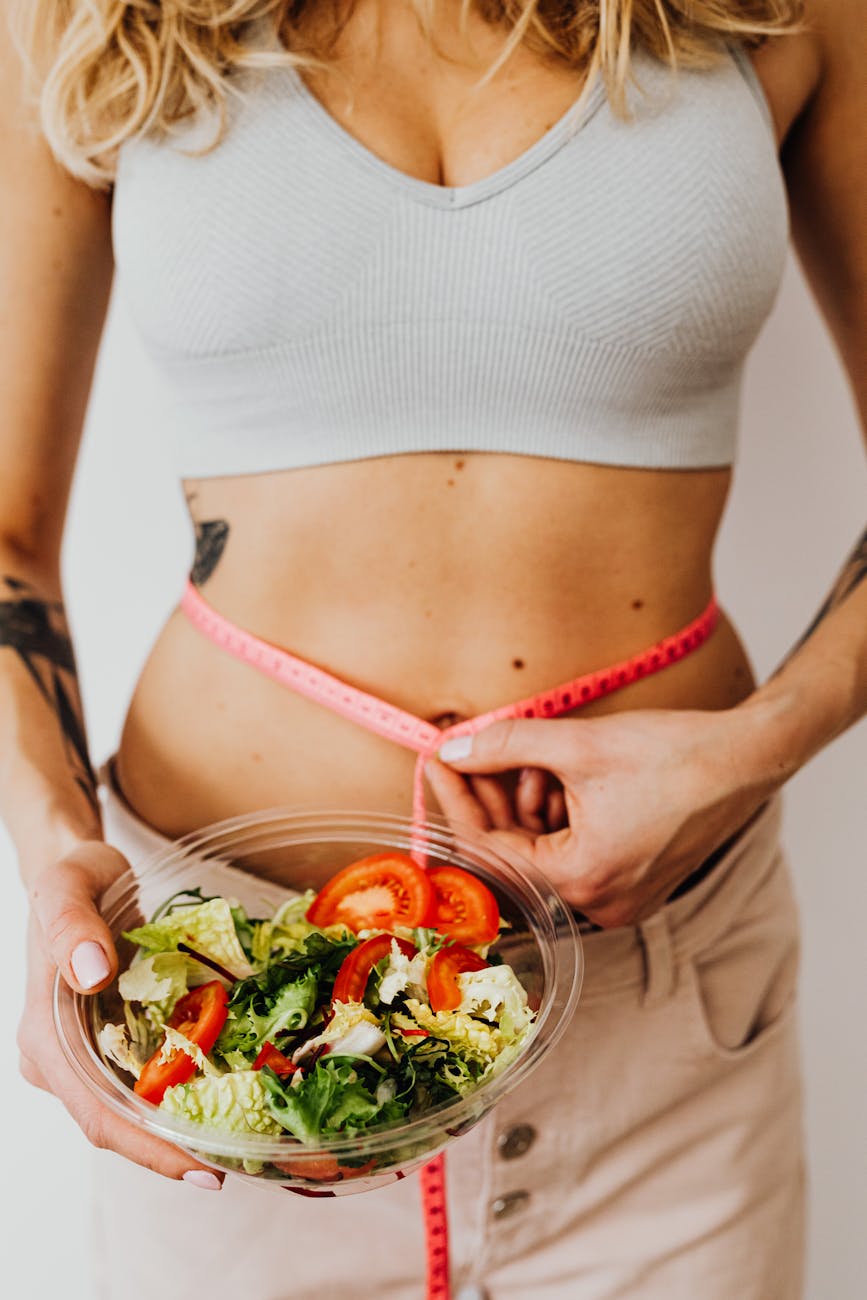 woman measuring her waistline while holding a bowl of salad